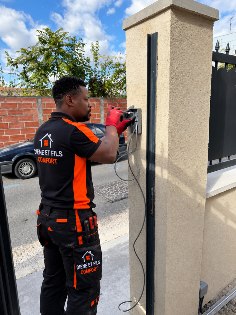 Électricien Diene et Fils Comfort installant un visiophone sur le pilier d’un portail, câble d’alimentation en attente