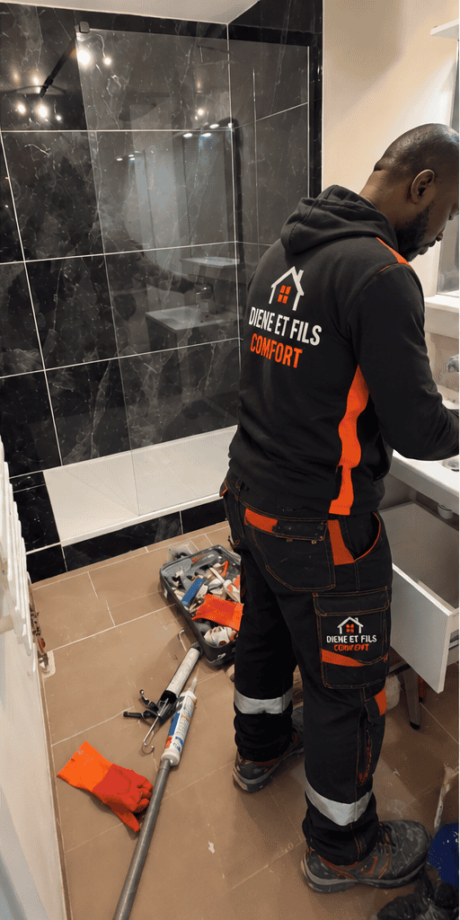 Plombier Diene et Fils Comfort posant un meuble vasque dans une salle de bain au carrelage effet marbre noir